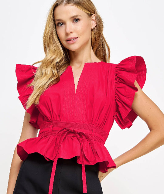 Woman wearing a red blouse with ruffled sleeves and black shorts on a white background