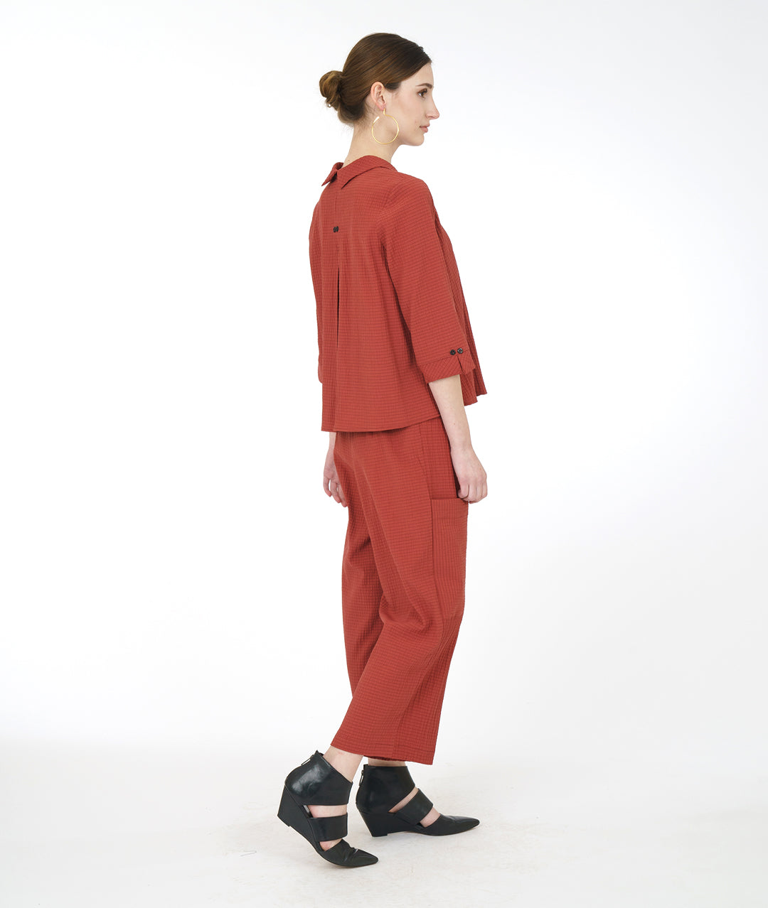 model in a sienna color pant with asymmetrical cargo pockets, worn with a matching button down top with 3/4 sleeves and a twin button detail up the front