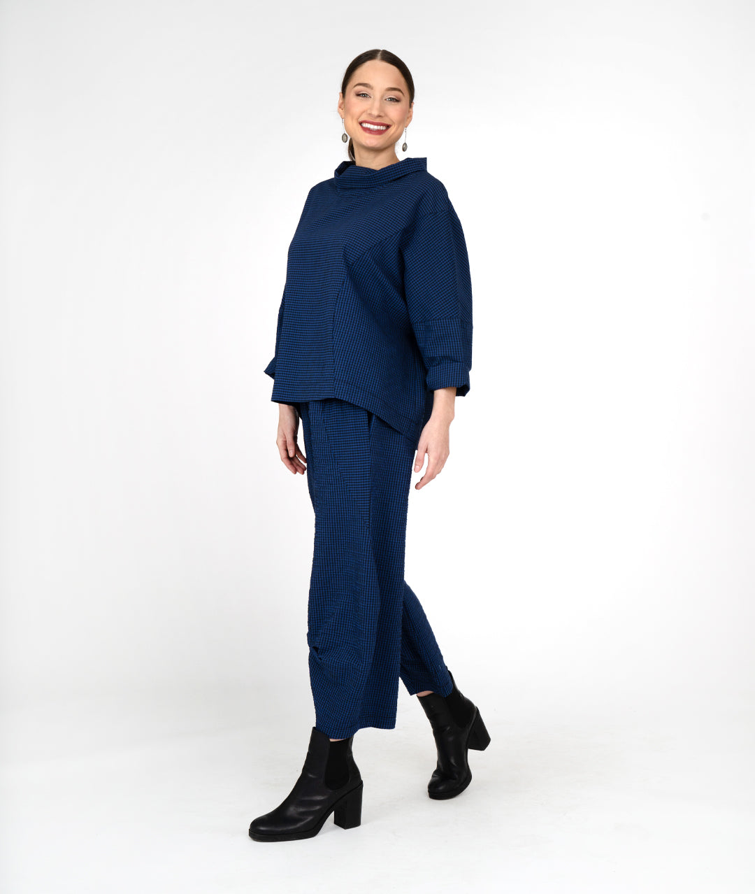 model in a black and blue striped wide leg pant, with a tuck detail at the ankles. Worn with a matching boxy top with a cowl neckline and long sleeves