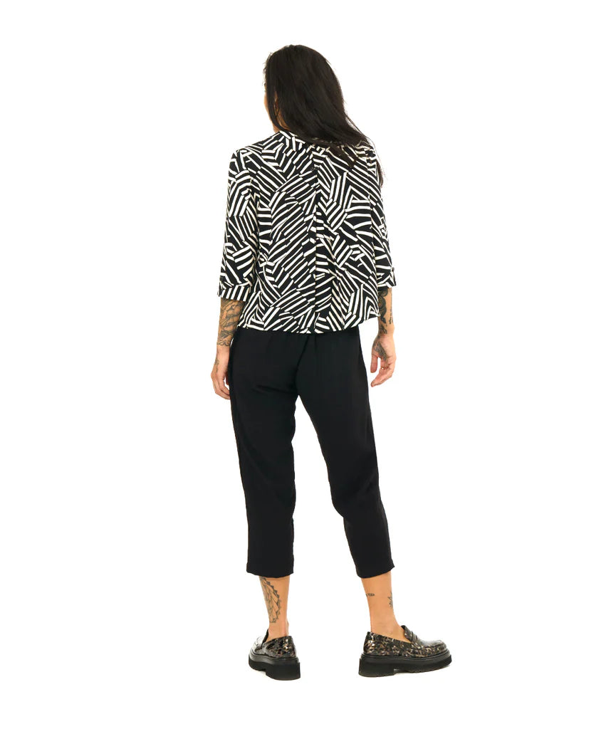 model showing back of black and white design button up 3/4 sleeve top, paired with black pants and loafers