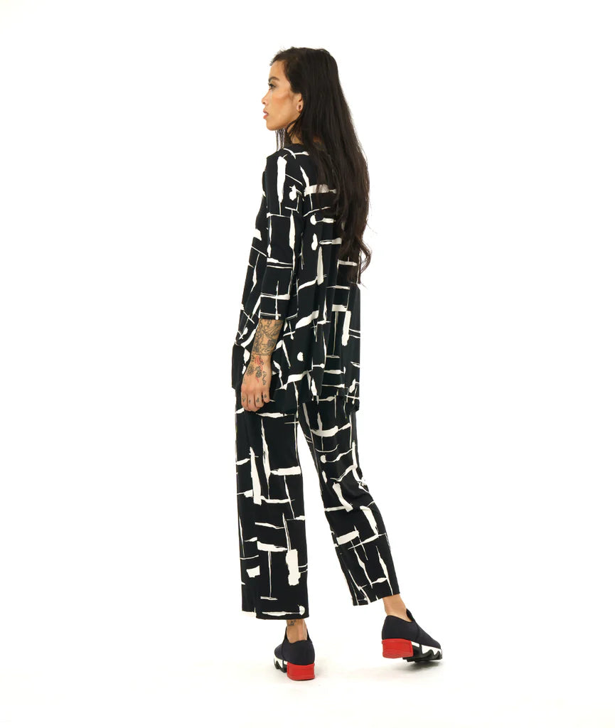 model wearing black and white print pullover top with a round neckline, 3/4 sleeves, and a wide hem with splits on either side, giving the illusion of a dipped hem with matching pants and black sneakers