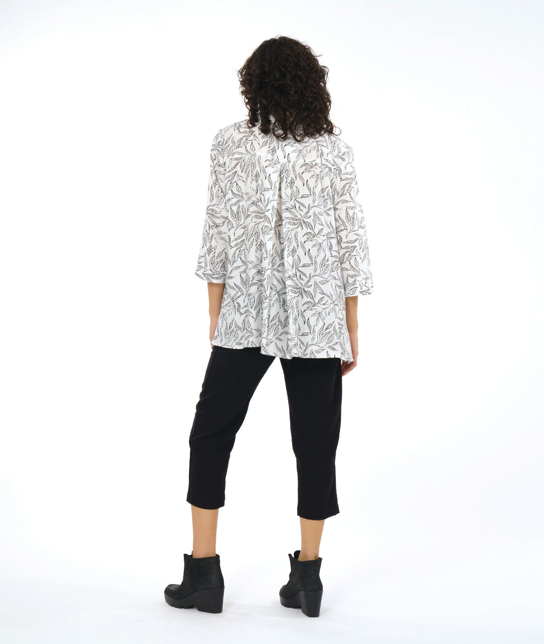 model in a slim black cropped pant, worn with a white button down blouse with a twinbutton detail, 3/4 sleeves, a long body and a floral print