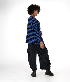 model in a black and blue striped top with a pocket at the waist seam, worn with a wide leg pant