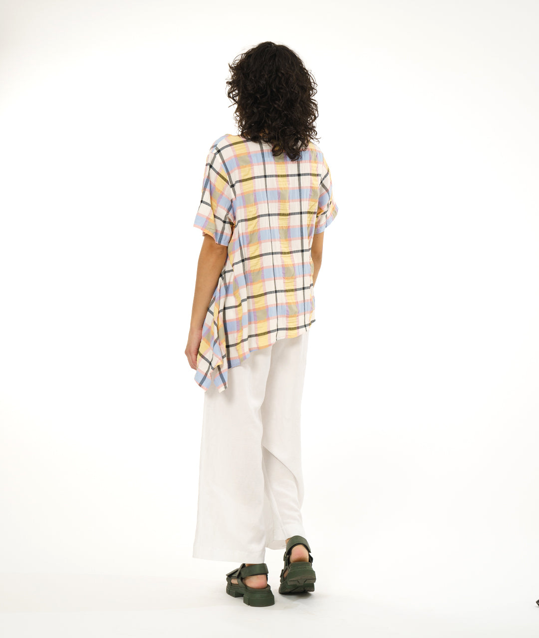 model in a wide leg white pant with an asymmetrical multi color plaid pullover top
