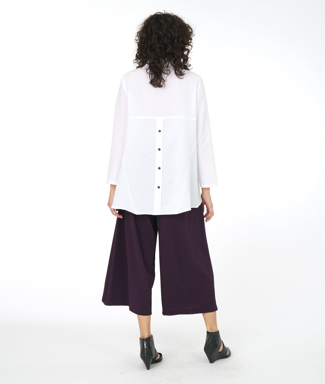 model in a long white button down blouse with a wide leg aubergine grid textured pant with an overlapping panel giving a skirt look