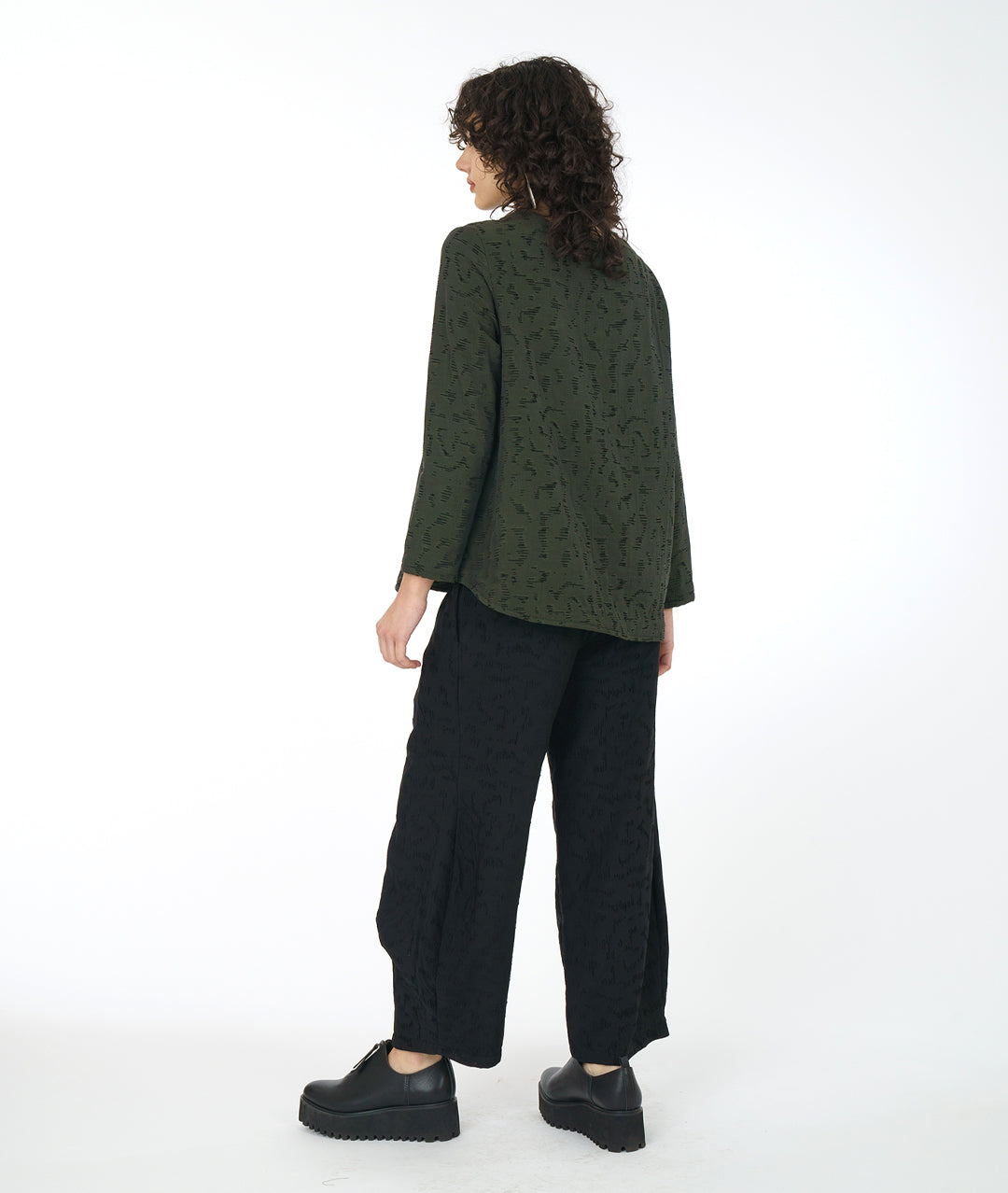 model in a wide leg black pant with a matching green pullover top with a rounded neckline, long sleeves, a boxy body and a triangular shaped false placket at the top, held with a single oversized button