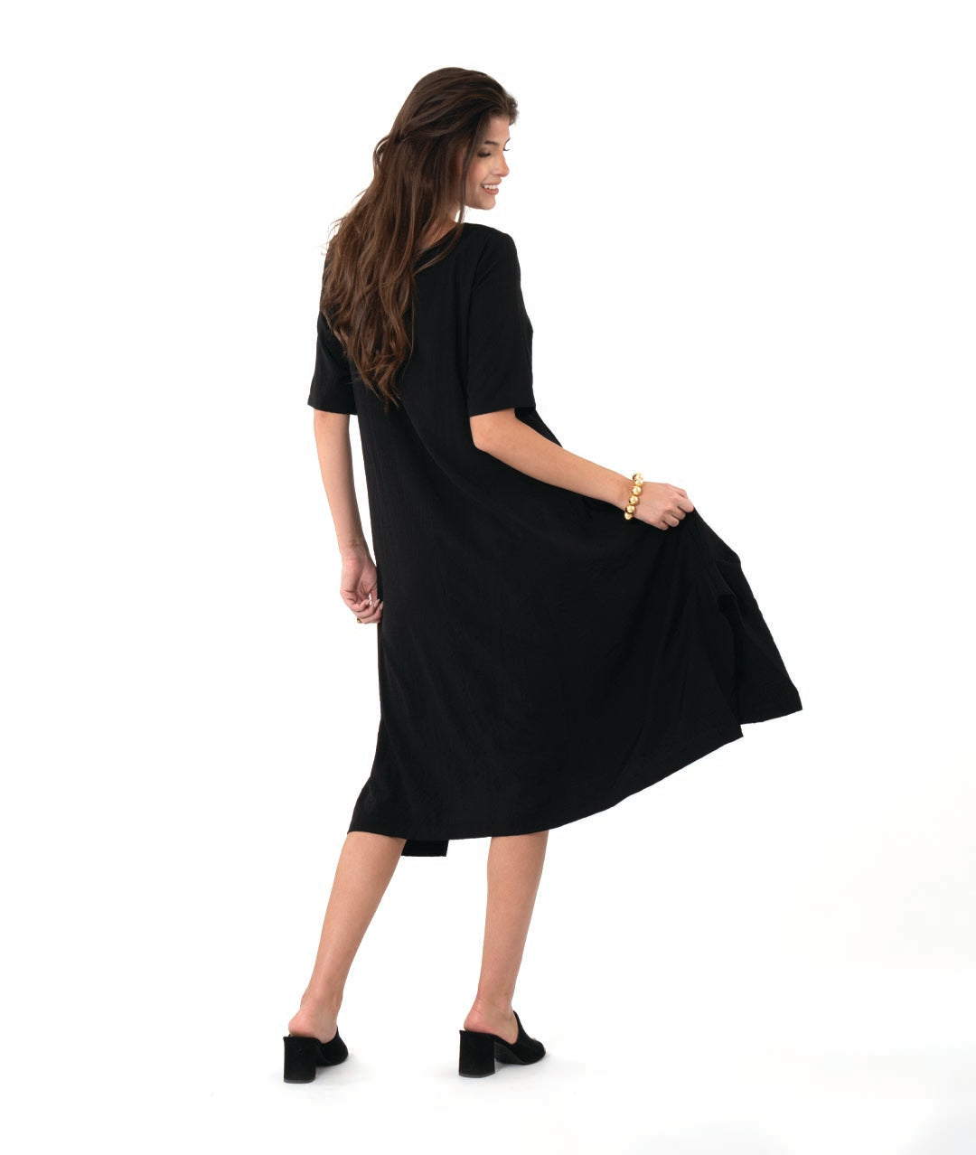 model in a pullover black dress with a slight grid texture. dress has a rounded neck, elbow length sleeves, and a flowy skirt with tucks and splits