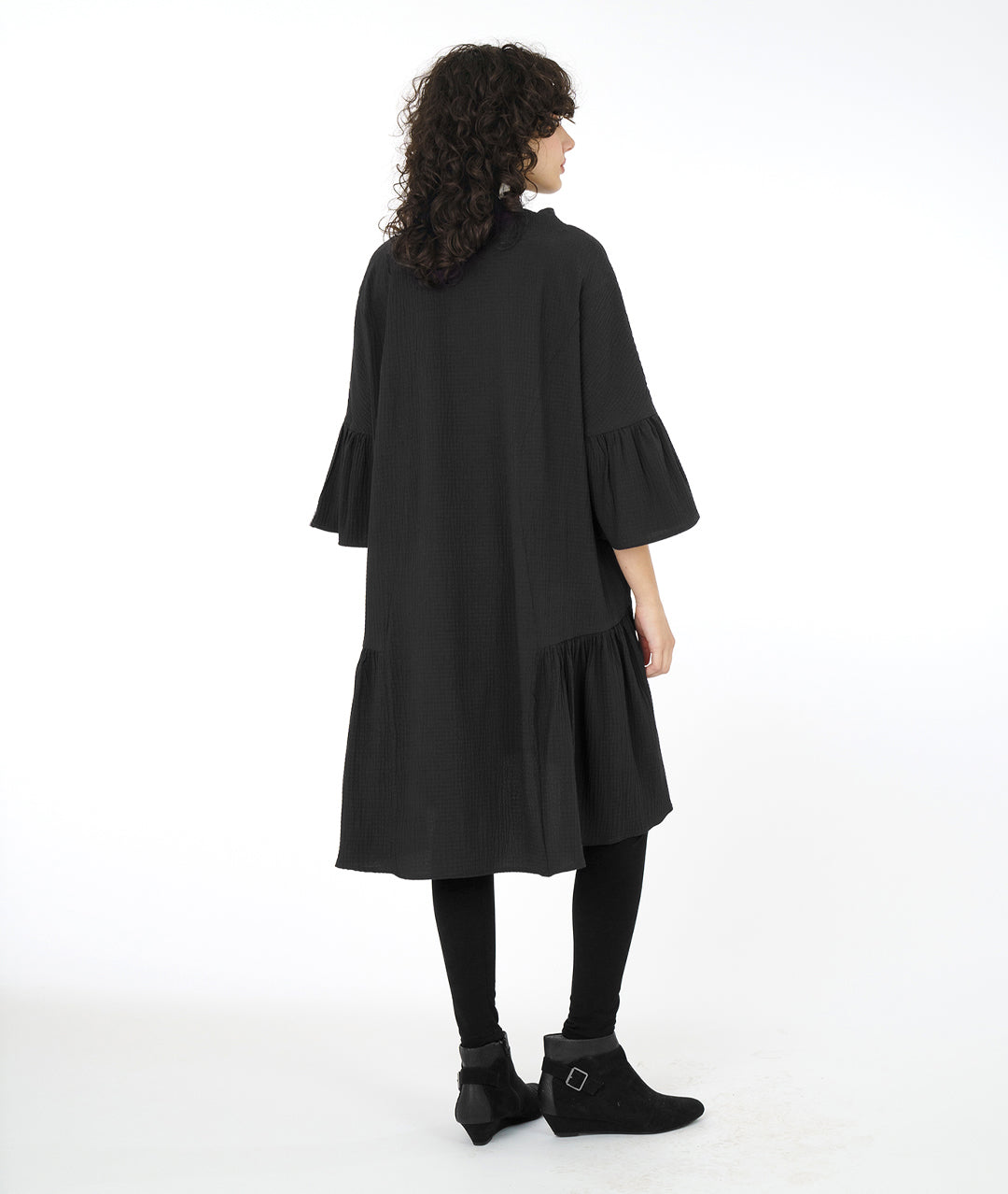 model in a black boxy dress with a cowl neck and a long ruffle at the skirt and sleeves