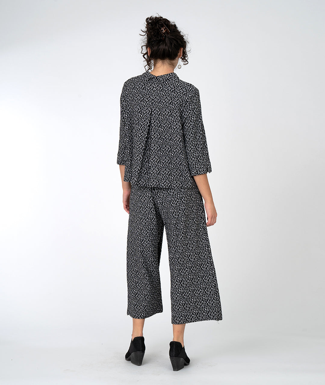 model in a wide leg black and grey leaf print pant with an overlapping front, worn with a matching button down with a twin button and 3/4 sleeves