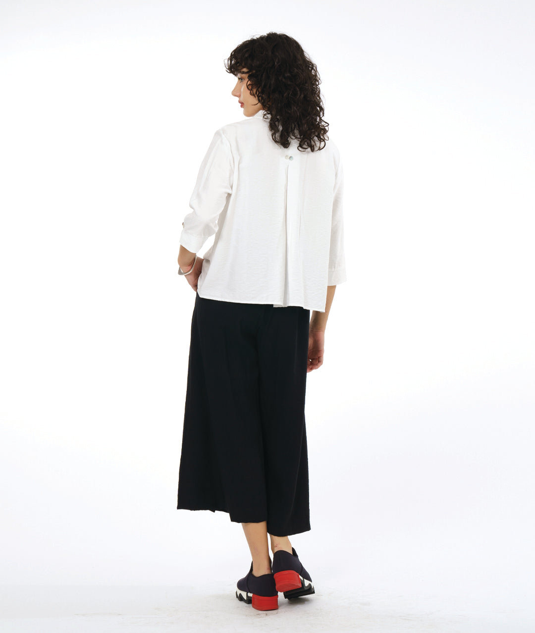 model in a black wide leg pant with overlapping apron panels in the front, worn with a white button down blouse with a twin button detail and 3/4 sleeves