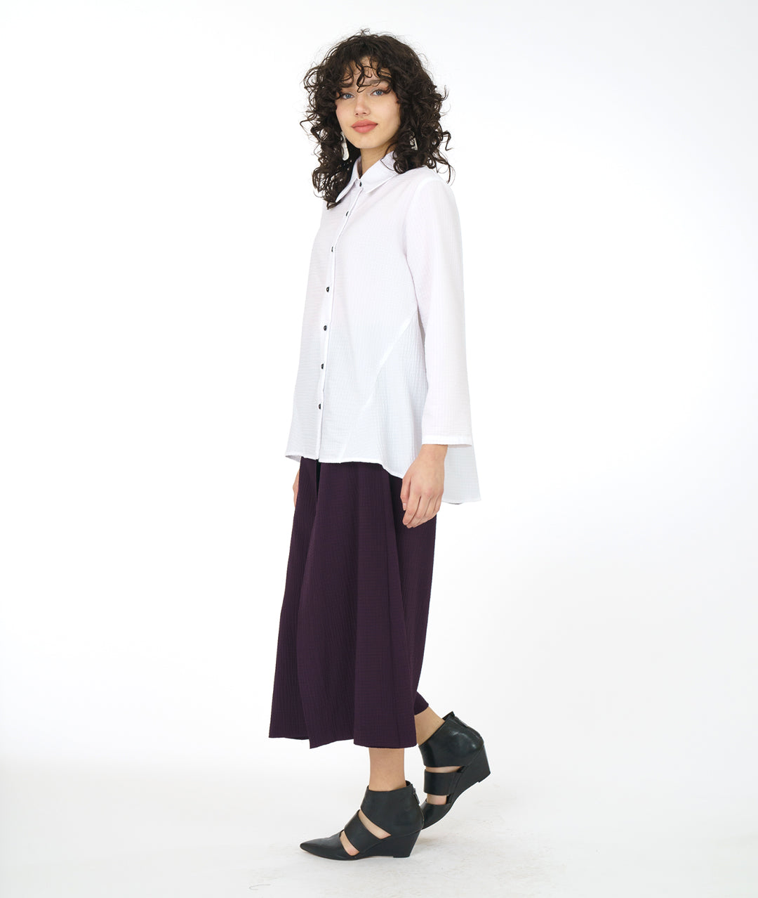 model in a long white button down blouse with a wide leg aubergine grid textured pant with an overlapping panel giving a skirt look