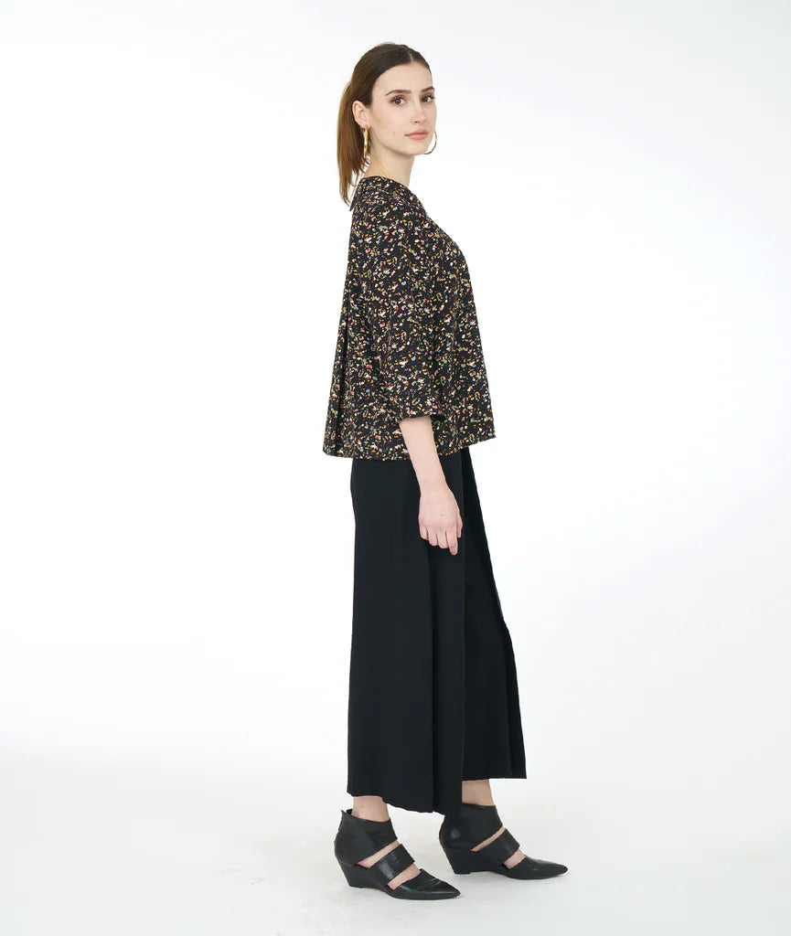 model wearing black terrazzo print top with double sets of "twin" buttons down the front, easy a-line shape and straight hem. sleeves are 3/4 sleeve with open cuff. inverted pleat and open notched collar in back. paired with black pants and shoes.