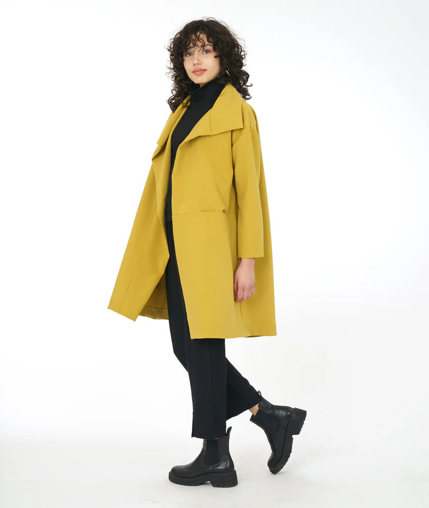 model in black pants and boots with a gold asymmetrical jacket with a large collar