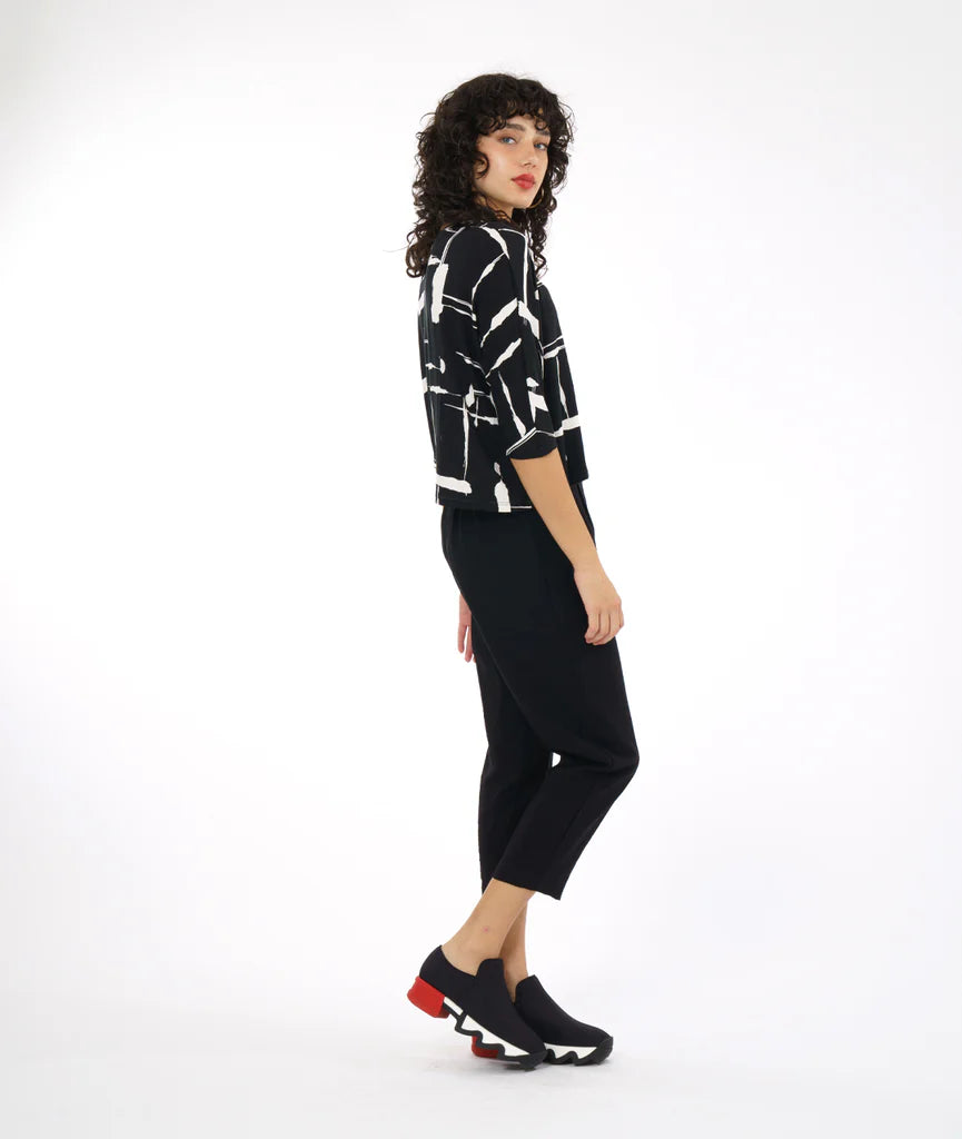 model wearing black and white print top with boxy cut, dolman sleeves, and a high neck paired with black pants and sneakers