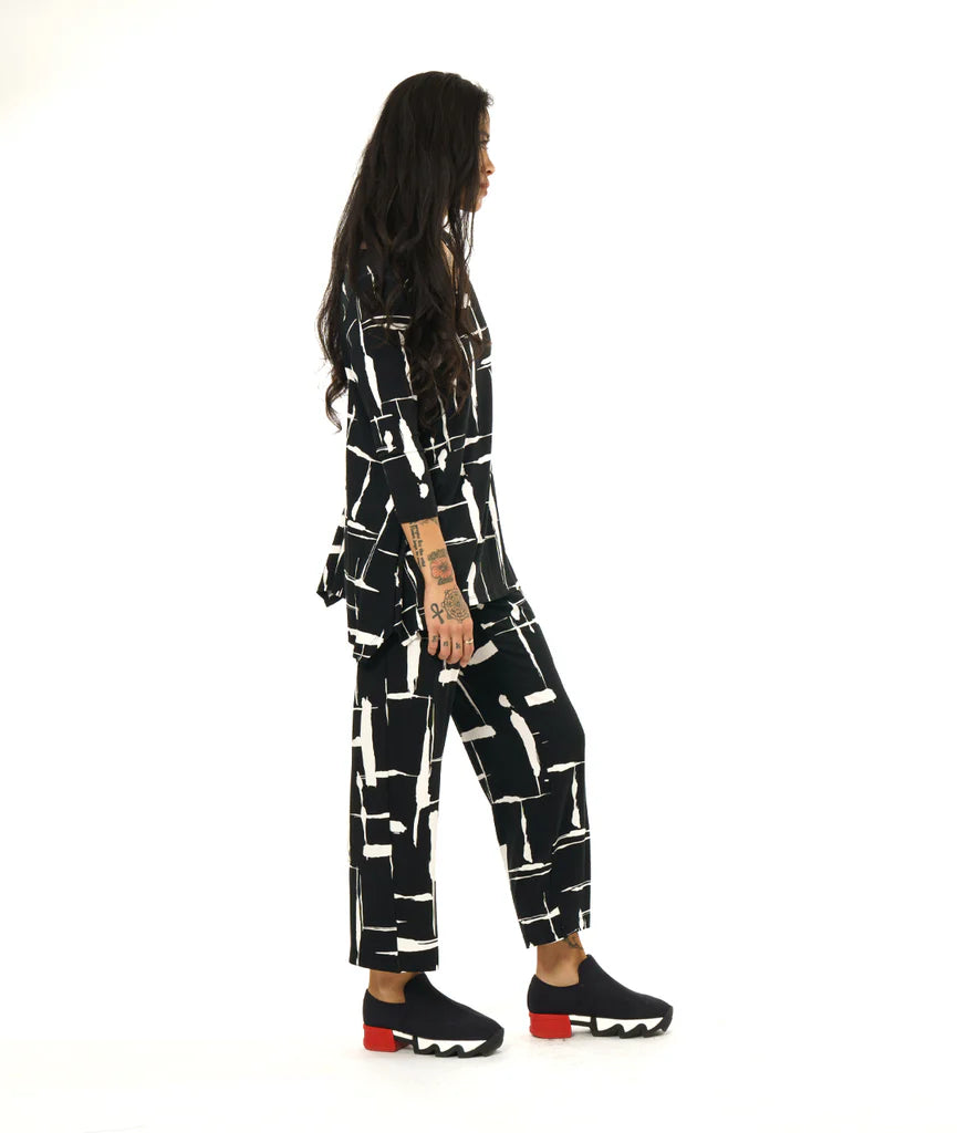 model wearing black and white print pullover top with a round neckline, 3/4 sleeves, and a wide hem with splits on either side, giving the illusion of a dipped hem with matching pants and black sneakers