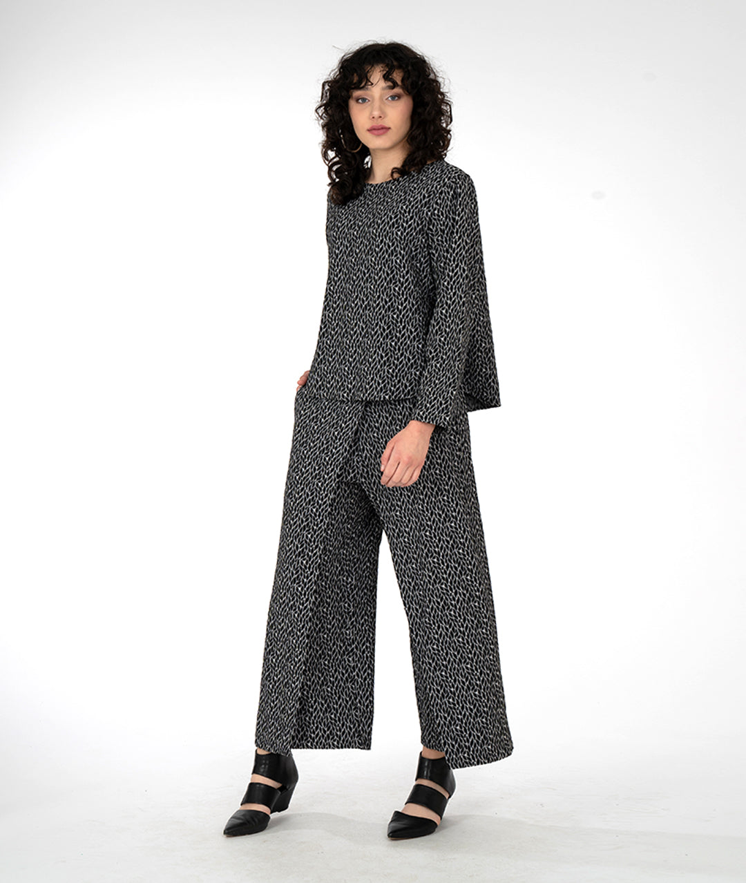 model in a wide leg grey and black leaf print pant with an overlapping front, worn with a matching pullover top with long sleeves and a high round neckline