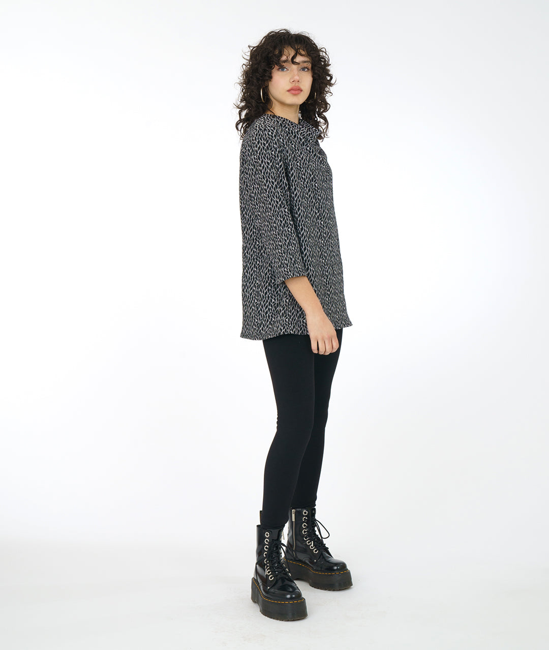 model in a black boot and legging, worn with a grey, black and white leaf print tunic with a 3/4 sleeve and a high cowl neck