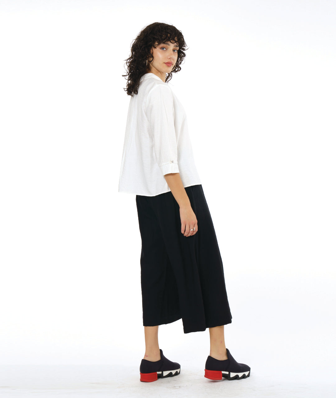 model in a black wide leg pant with overlapping apron panels in the front, worn with a white button down blouse with a twin button detail and 3/4 sleeves