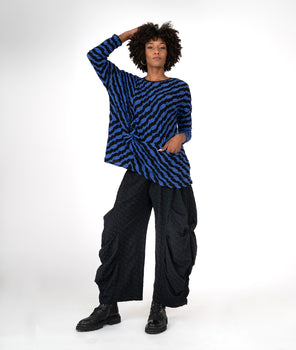 model in a black and blue striped top with a pocket at the waist seam, worn with a wide leg pant