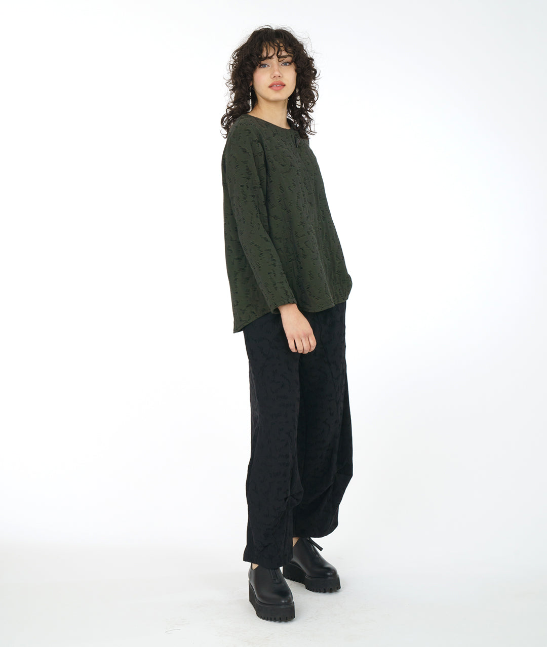 model in a wide leg black pant with a matching green pullover top with a rounded neckline, long sleeves, a boxy body and a triangular shaped false placket at the top, held with a single oversized button