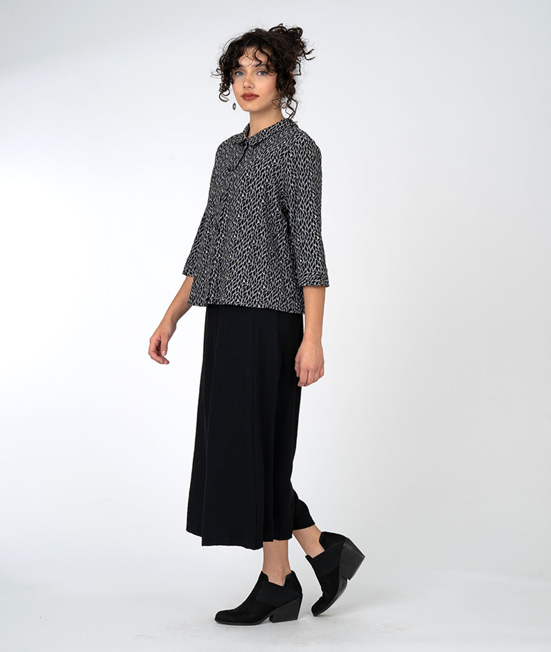 model in a wide leg black pant with an overlapping front, worn with a black and grey leaf print button down with a twin button and 3/4 sleeves