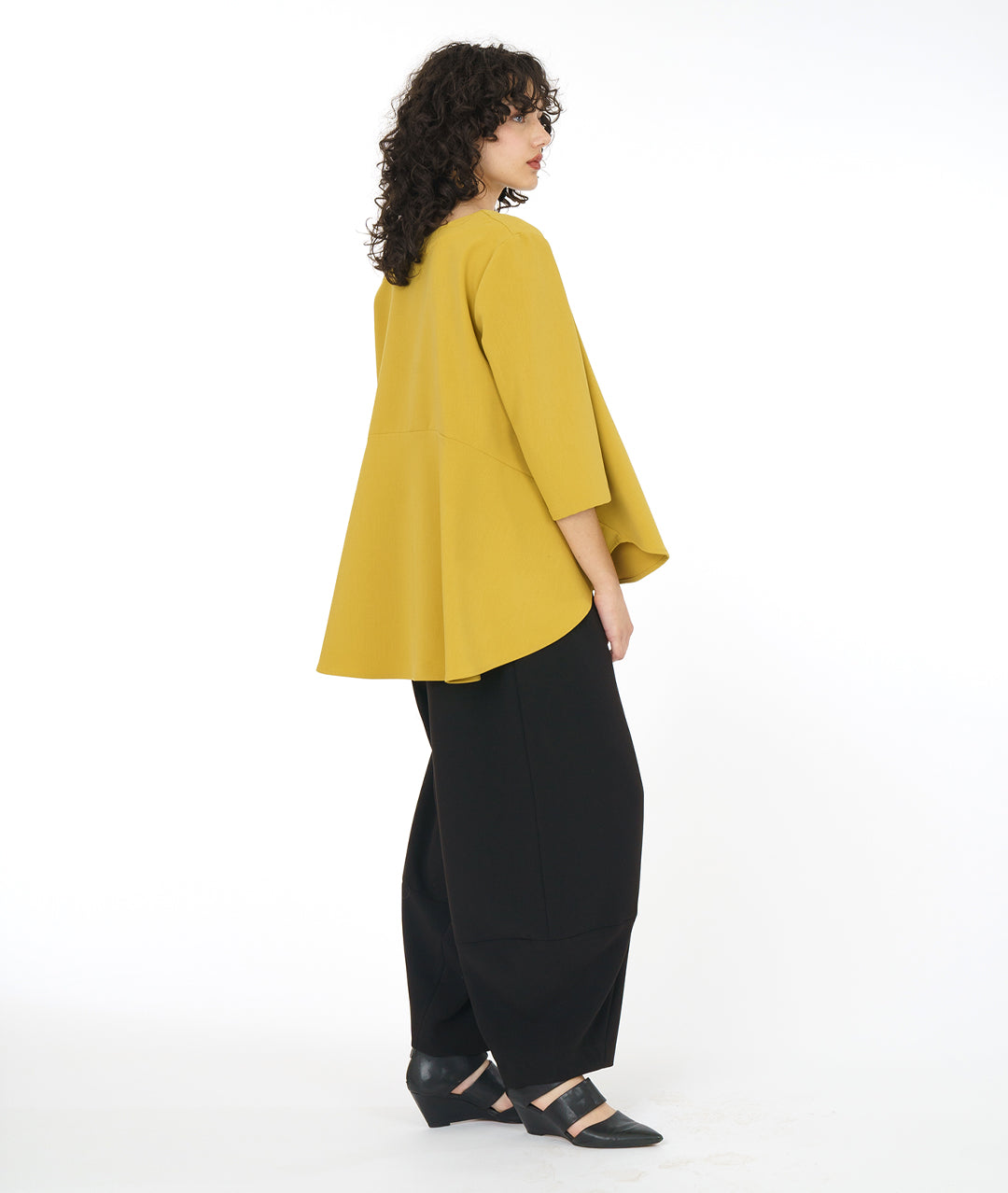 model in a high-low hemmed gold pullover top, with a black pant with a full leg tapering down at the ankle