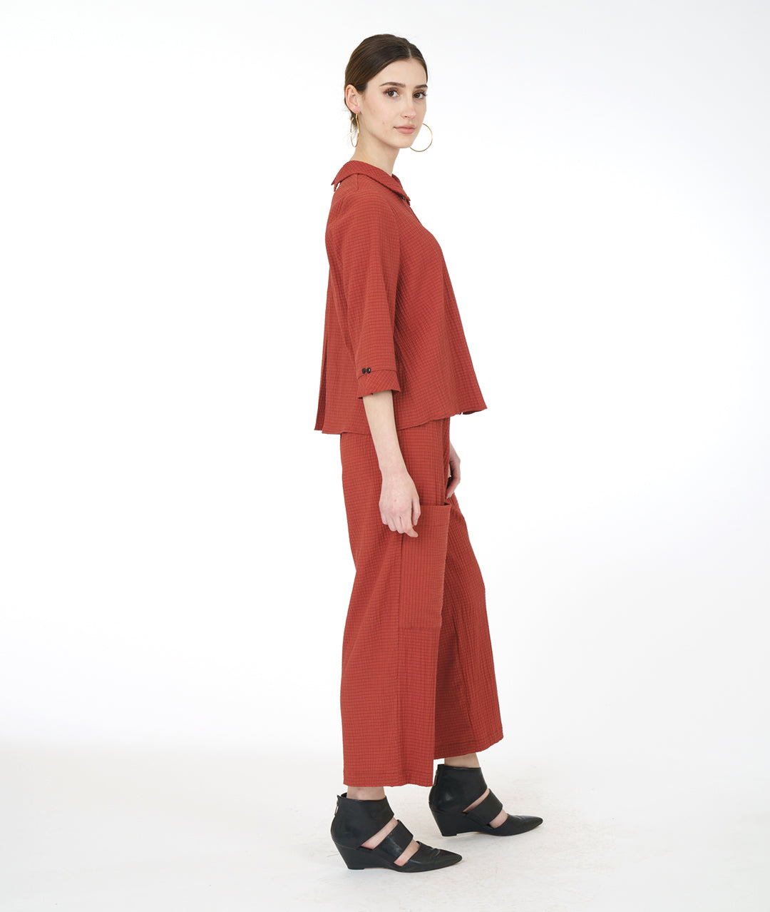 model in a sienna color pant with asymmetrical cargo pockets, worn with a matching button down top with 3/4 sleeves and a twin button detail up the front
