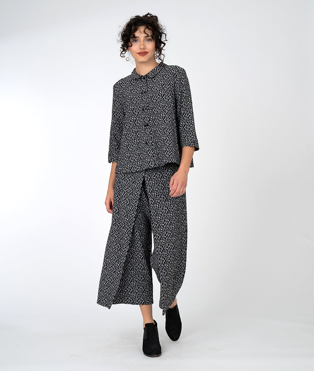 model in a wide leg black and grey leaf print pant with an overlapping front, worn with a matching button down with a twin button and 3/4 sleeves