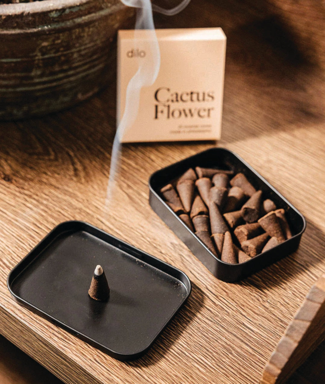 an open container of cactus flower scented incense cones, with one lit