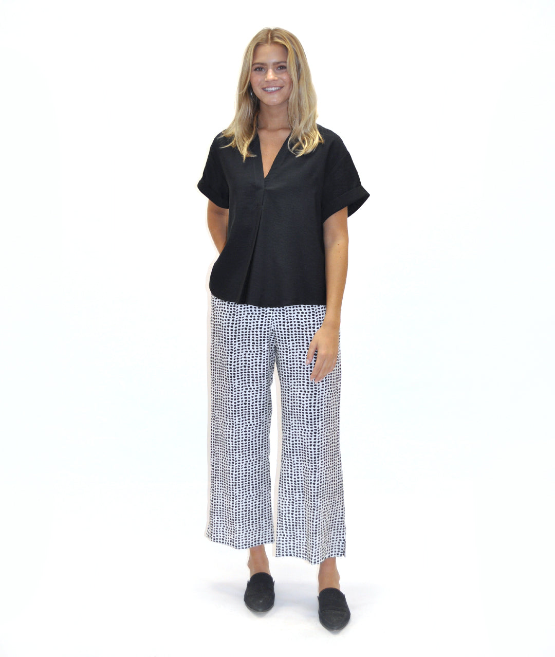model in a black a white dot print pant with a solid black top with a vneck and pleat down the center front