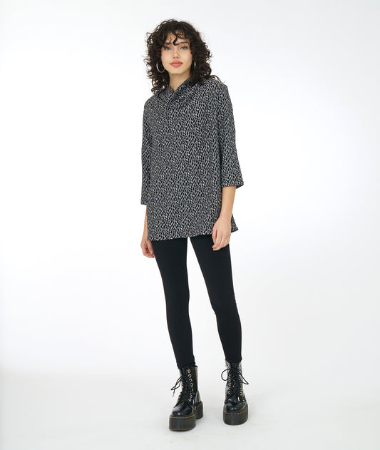 model in a black boot and legging, worn with a grey, black and white leaf print tunic with a 3/4 sleeve and a high cowl neck