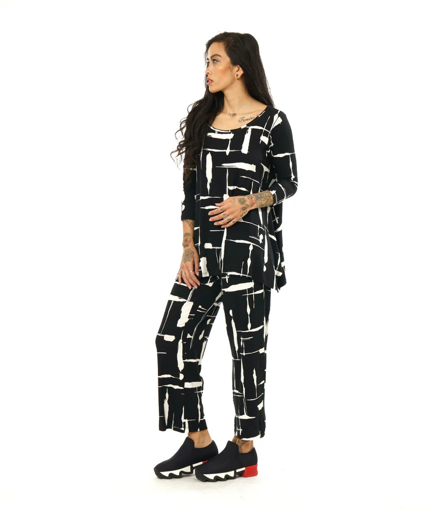 model wearing black and white print pullover top with a round neckline, 3/4 sleeves, and a wide hem with splits on either side, giving the illusion of a dipped hem with matching pants and black sneakers