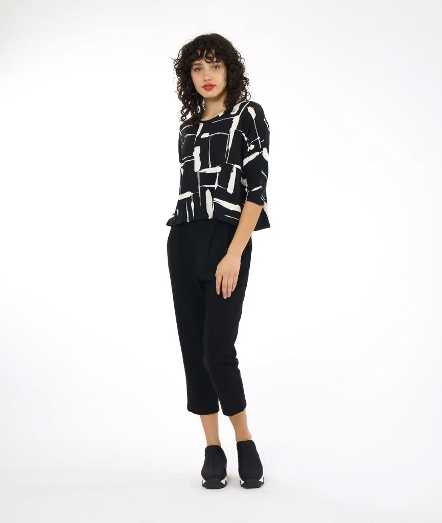 model wearing black and white print top with boxy cut, dolman sleeves, and a high neck paired with black pants and sneakers