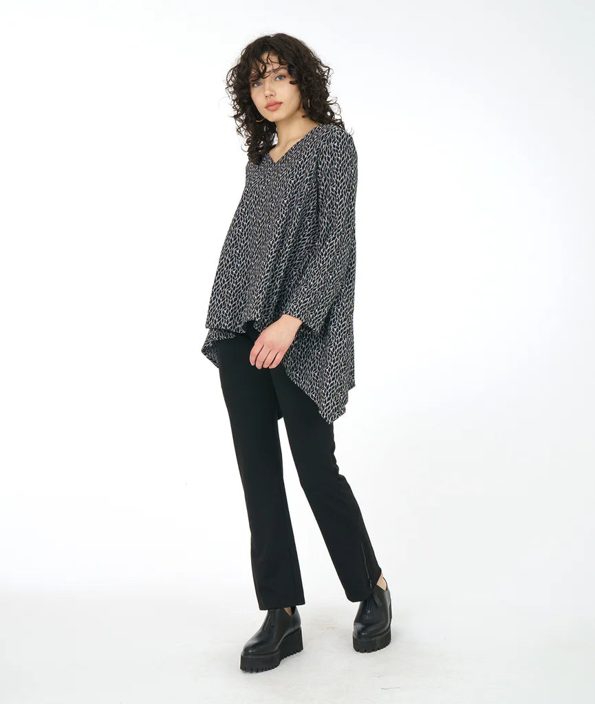 model wearing top in leaf with clean round neckline, straight hem across the front, and longer bias cut points on the back. sleeves go just past the elbow. paired with black pants and shoes. 