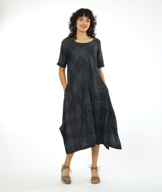 model in a midi length dress with short sleeves, a round neckline and tucks at the sides. dress has a large grid print on shades of deep gray with multi directional panels