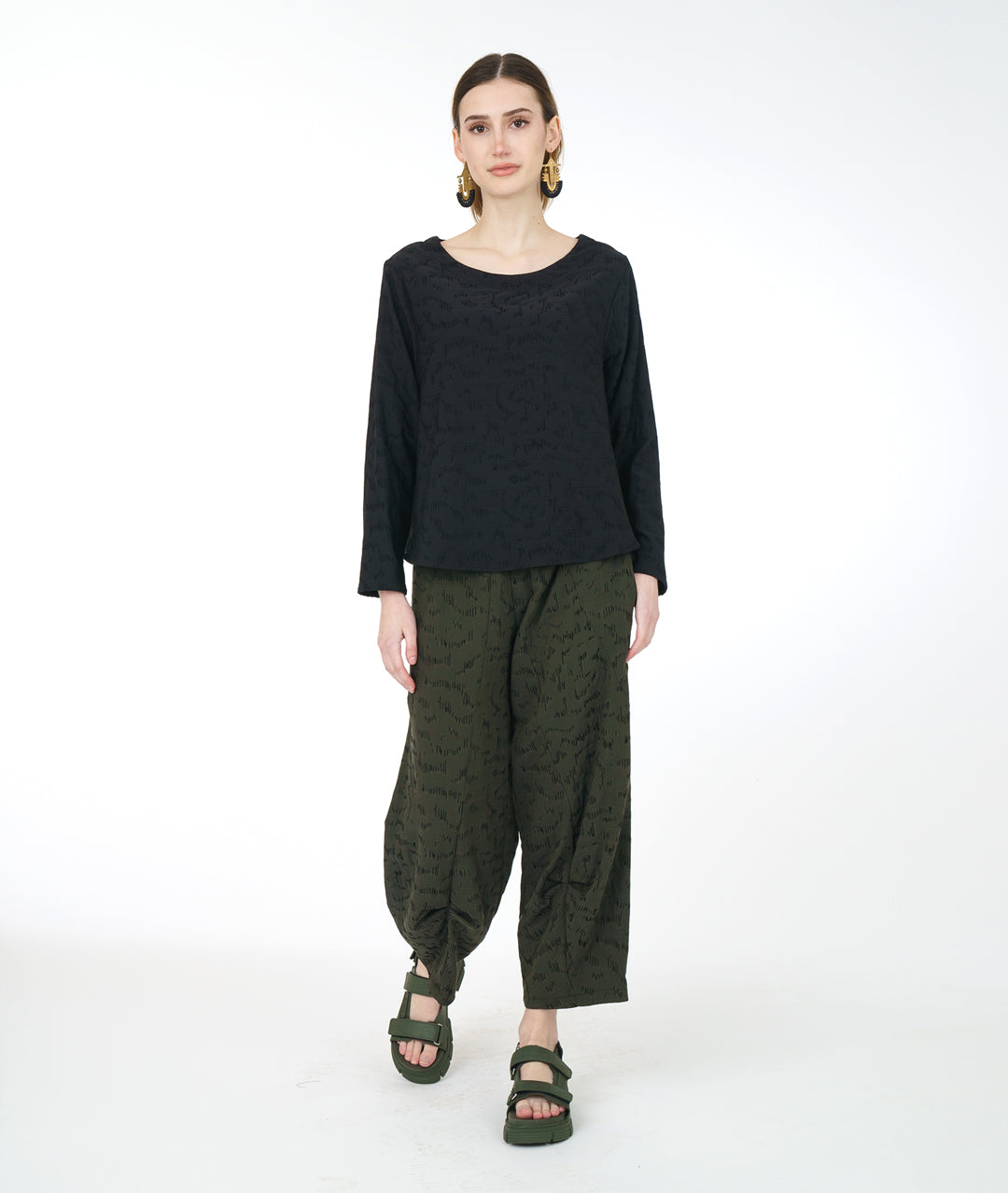 model in a wide leg green pant with a matching black pullover top with a rounded neckline, long sleeves, a boxy body and darts at the bust