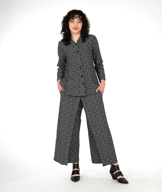 model in a wide leg grey and black leaf print pant with an overlapping front, worn with matching button down blouse with a standing collar and long sleeves
