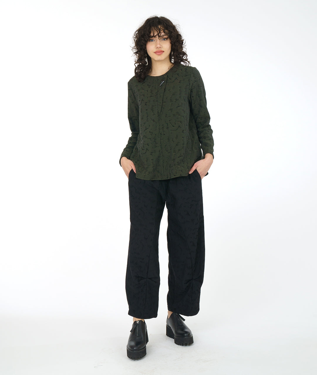 model in a wide leg black pant with a matching green pullover top with a rounded neckline, long sleeves, a boxy body and a triangular shaped false placket at the top, held with a single oversized button