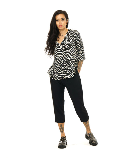 model in a black and white broken stripe print pullover top with 3/4 sleeves and a v-neck. worn with a simple black crop pant