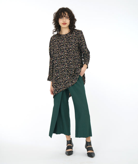 model in a wide leg forrest green pant with a black terrazzo print top. Top is asymmetrical with a drape and cocoon sleeve on one side only