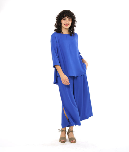 model in a wide leg periwinkle pant with a side slit on either side, worn with a matching pullover top with 3/4 sleeves and a rounded hem, dipping lower in the back
