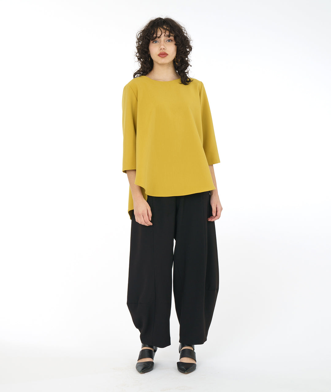 model in a high-low hemmed gold pullover top, with a black pant with a full leg tapering down at the ankle