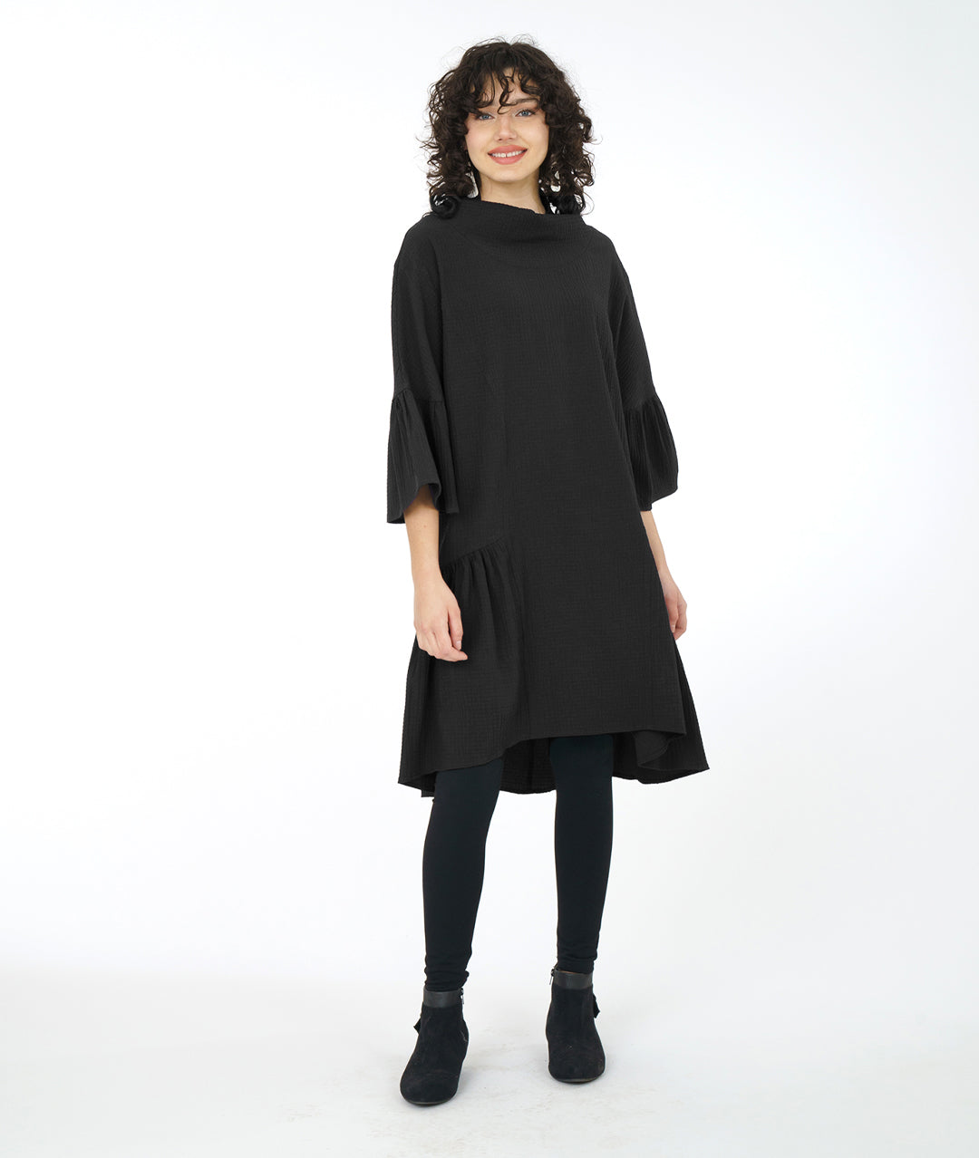 model in a black boxy dress with a cowl neck and a long ruffle at the skirt and sleeves