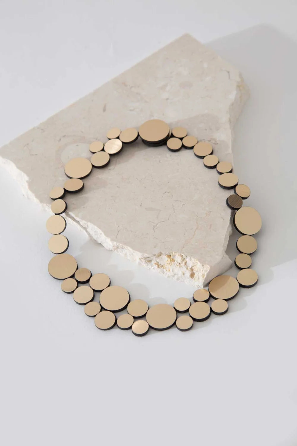 Gold circle cluster necklace laying on rock against white background
