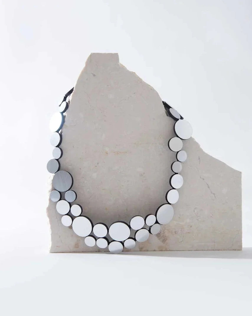 Silver circle cluster necklace on rock against white background