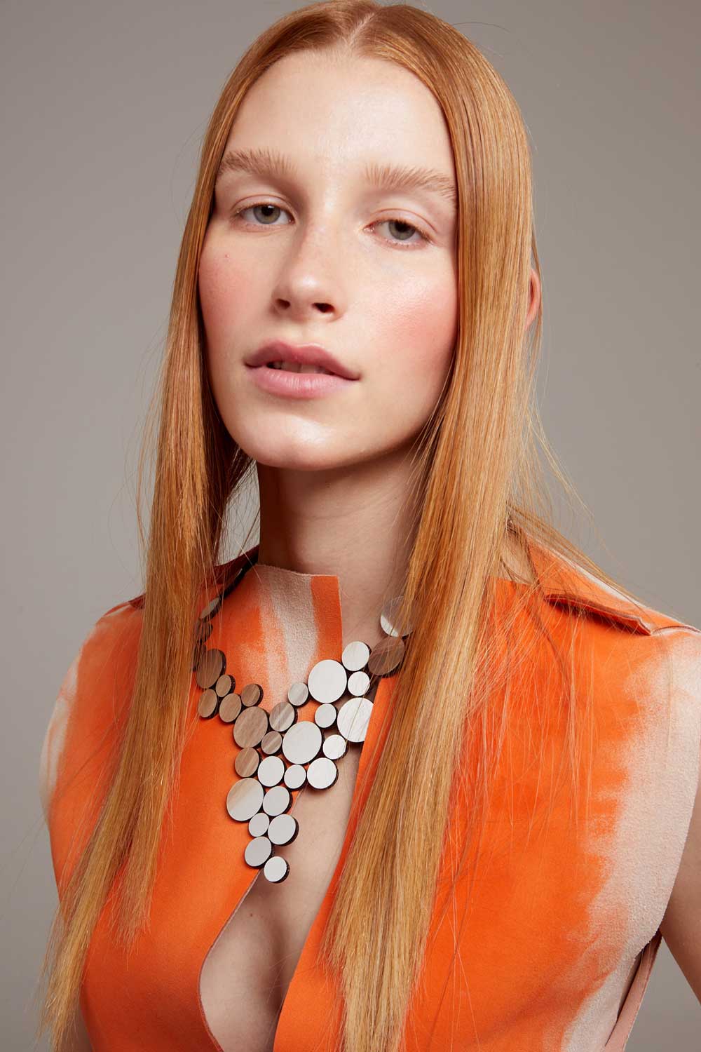 model wearing silver circle cluster necklace with orange top against grey background