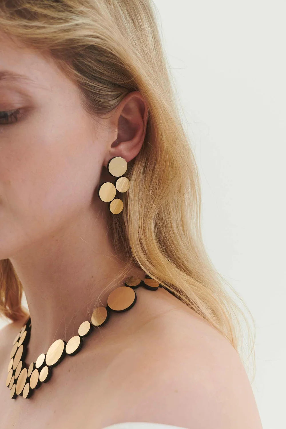 model wearing gold circle cluster earrings and necklace against white background