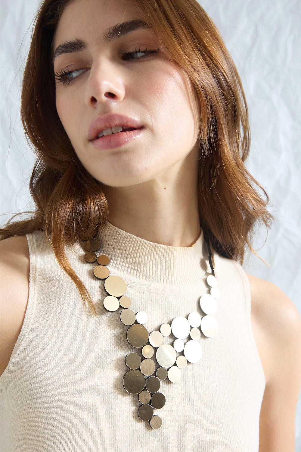 model wearing gold circle cluster necklace with beige top against white background