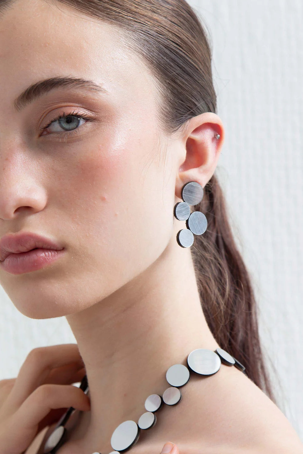 model wearing silver circle cluster earrings and necklace against white background