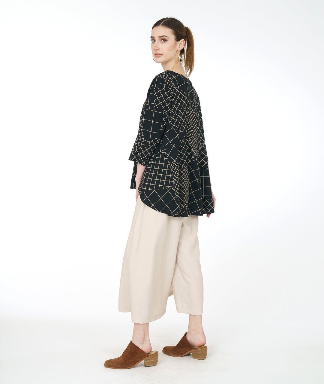model in a wide leg ivory pant with a black and ivory grid print pull over top with a high-low hem, 3/4 sleeves and a full bodied back